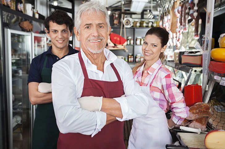 Senior man smiling with young couple behind, in storeroom of restaurant