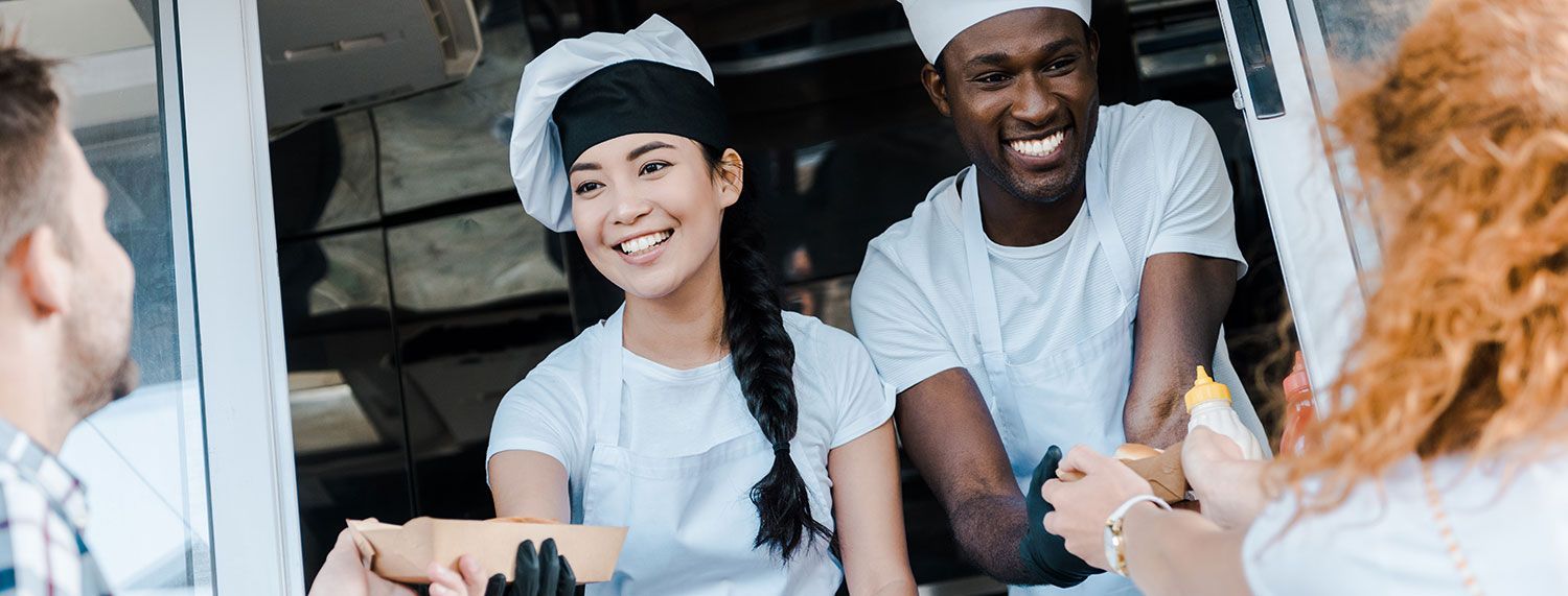 smiling Asian woman and black man working in food truck